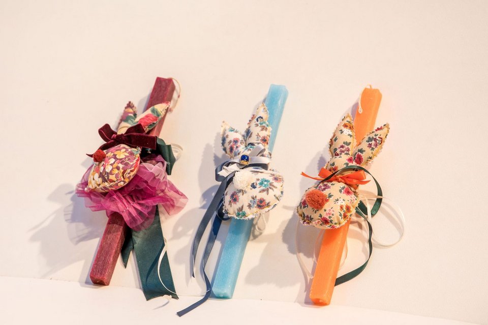 Στο επίκεντρο της φετινής συλλογής βρίσκονται οι χειροποίητες πασχαλινές λαμπάδες, όλες φτιαγμένες στα εργαστήρια του Θεάτρου από το Τμήμα Ραπτικής