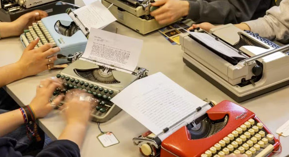 Σε μια αίθουσα διδασκαλίας, που θυμίζει σκηνή από τη δεκαετία του 1950, φοιτητές σκύβουν πάνω από μηχανικές γραφομηχανές, πατώντας τα πλήκτρα με αβεβαιότητα και ακούγοντας το χαρακτηριστικό «ντινγκ» στο τέλος κάθε γραμμής / ΑΡ