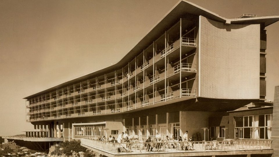 Η ιστορία του ξεκινά το 1961, όταν εγκαινιάστηκε ως πολυτελές ξενοδοχείο του Ελληνικού Οργανισμού Τουρισμού, σχεδιασμένο από τον Παύλο Μυλωνά ως σύμβολο της μεταπολεμικής αισιοδοξίας της χώρας / WIKIPEDIA