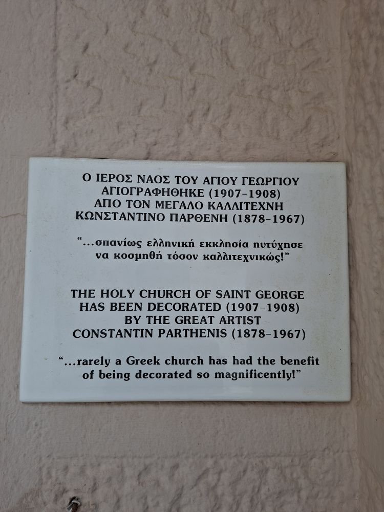 «…Σπανίως ελληνική εκκλησία ηυτύχησε να κοσμηθή τόσον καλλιτεχνικώς!» Ο Ιερός Ναός του Αγίου Γεωργίου αγιογραφήθηκε από τον Κωνσταντίνο Παρθένη, γράφει η πινακίδα. / φωτογραφία iefimerida 