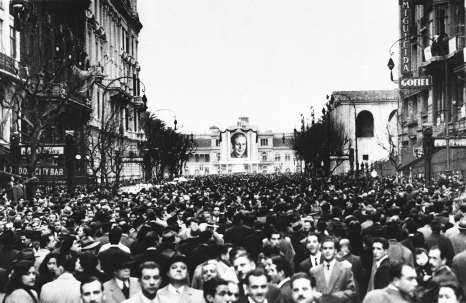 Χιλιάδες Αργεντινοί έχουν κατακλύσει τη λεωφόρο Αβενίδα ντε Μάγιο στο Μπουένος Άιρες, για να αποχαιρετήσουν την Εύα Περόν, στις 27 Ιουλίου 1952. Στο βάθος διακρίνεται μια τεράστια φωτογραφία της, καλυμμένη με μαύρο ύφασμα
