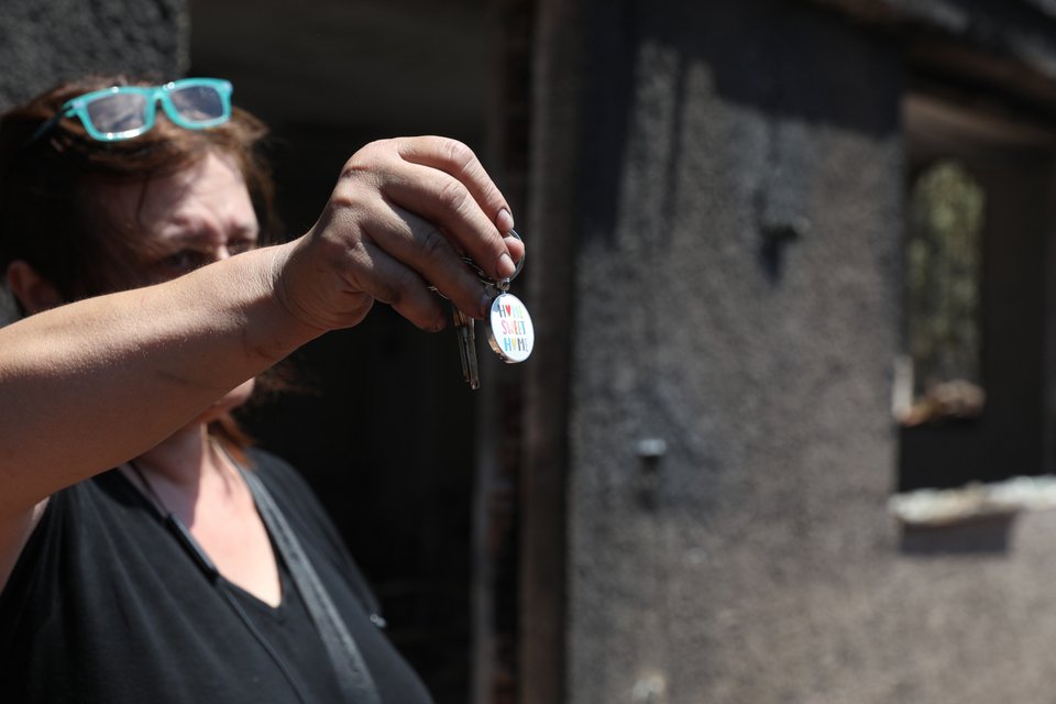 Γυναίκα σε καμένο σπίτι δείχνει στον φακό μπρελόκ με το μήνυμα «Σπίτι μου σπιτάκι μου» / Eurokinissi