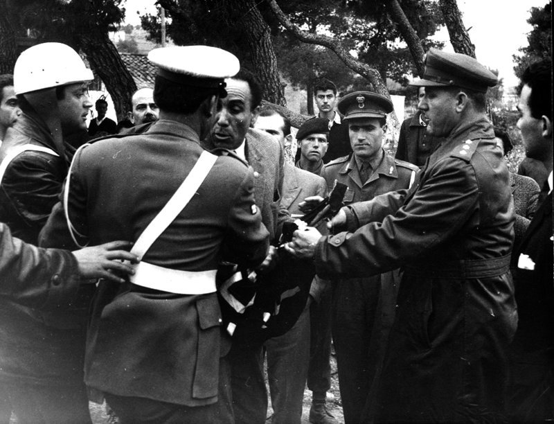 Αστυνομικοί προσπαθούν να πάρουν το πανό από τα χέρια του Γρηγόρη Λαμπράκη.Όταν τελικά το παίρνουν, ο Λαμπράκης συνεχίζει βάζοντας στο στήθος του, την αφίσα της Πορείας.