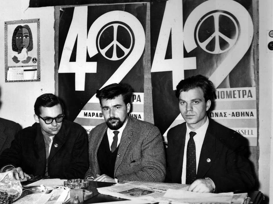 ΣΤΑ ΓΡΑΦΕΙΑ ΤΟΥ ΣΥΝΔΕΣΜΟΥ ΡΑΣΕΛ, στην οδο Ασκληπιού 3. Από αριστερά : Ο Νίκος Κιάος (Αντιπρόεδρος του Συνδέσμου), ο Πατ Ποτλ (Γραμματέας του Μπέρτραντ Ράσελ) και ο Μιχάλης Περιστεράκης (Πρόεδρος του Συνδέσμου). Έχουν πίσω τους τις αφίσες της Πορείας που αναγράφουν τον αριθμό των 42 χιλιομέτρων, όση είναι δηλαδή η απόσταση Μαραθώνα-Αθήνα .
