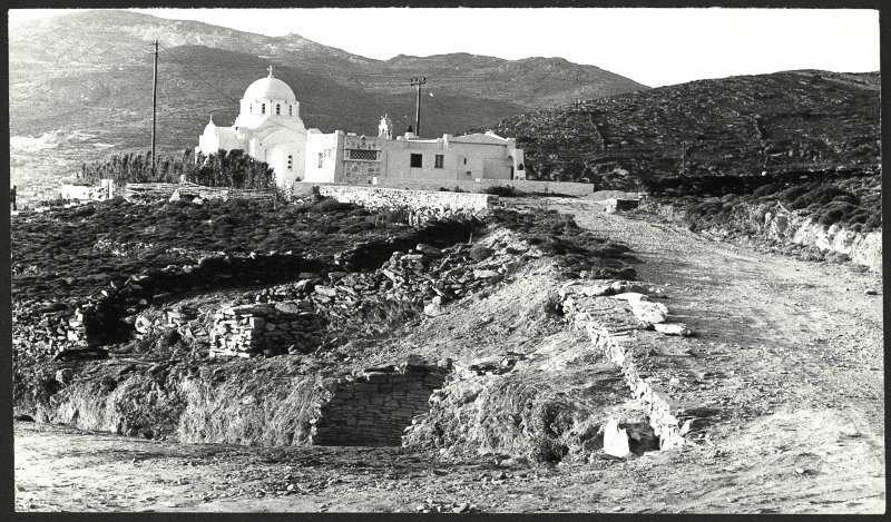 Άποψη της ανασκαφής στην Αγία Θέκλα, στην Τήνο, το 1979. Διακρίνονται τα υπολείμματα του θολωτού τάφου (κάτω) και η ομώνυμη εκκλησία (πάνω). © Αρχείο της εν Αθήναις Αρχαιολογικής Εταιρείας