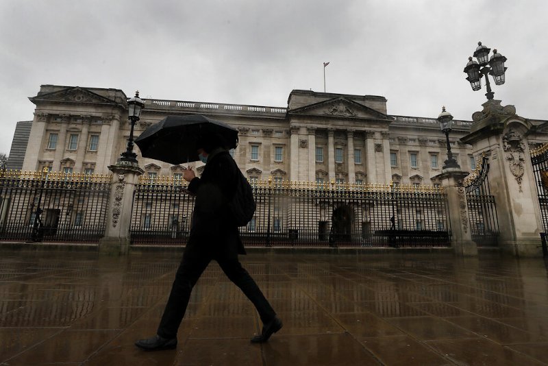 άνδρας με ομπρέλα περπατά έξω από το Παλάτι του Μπάκιγχαμ