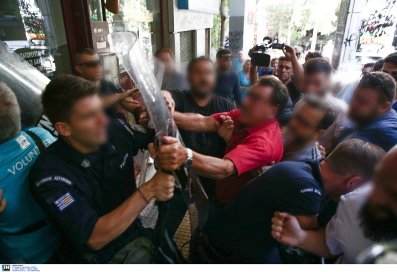 Αντρας με κόκκινη μπλούζα κρατά ασπίδα αστυνομικού