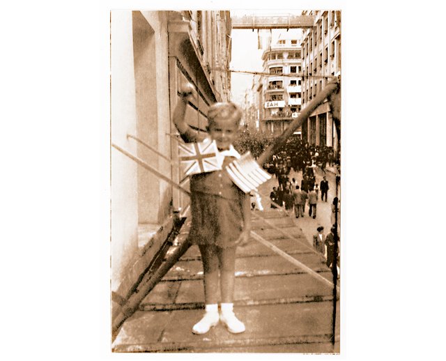 2 Οκτωβρίου 1944, οδός Αμερικής 1. Ο συγγραφέας Γ.Β. Δερτιλής εις νεαράν ηλικίαν πανηγυρίζει για την εκκένωση της Αθήνας από τα ναζιστικά στρατεύματα κατοχής και την είσοδο συμμαχικών στρατευμάτων στην πρωτεύουσα. Στο βάθος, στη γωνία Αμερικής και Πανεπιστημίου, η επιγραφή υπενθυμίζει στους συμμάχους την παρουσία του ΕΑΜ. H fφωτογραφία από το εξώφυλλο του βιβλίου του Γ.Β. Δερτιλή «Συνειρμοί, μαρτυρίες, μυθιστορίες» Εκδόσεις Πόλις