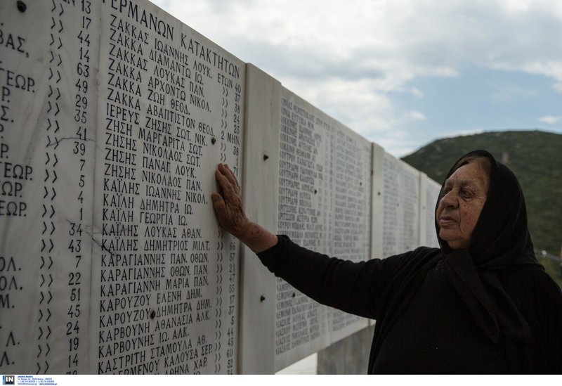 Μια ηλικιωμένη μαυροφορεμένη γυναίκα στη μαρμάρινη στήλη με τα ονόματα των θυμάτων στο Δίστομο