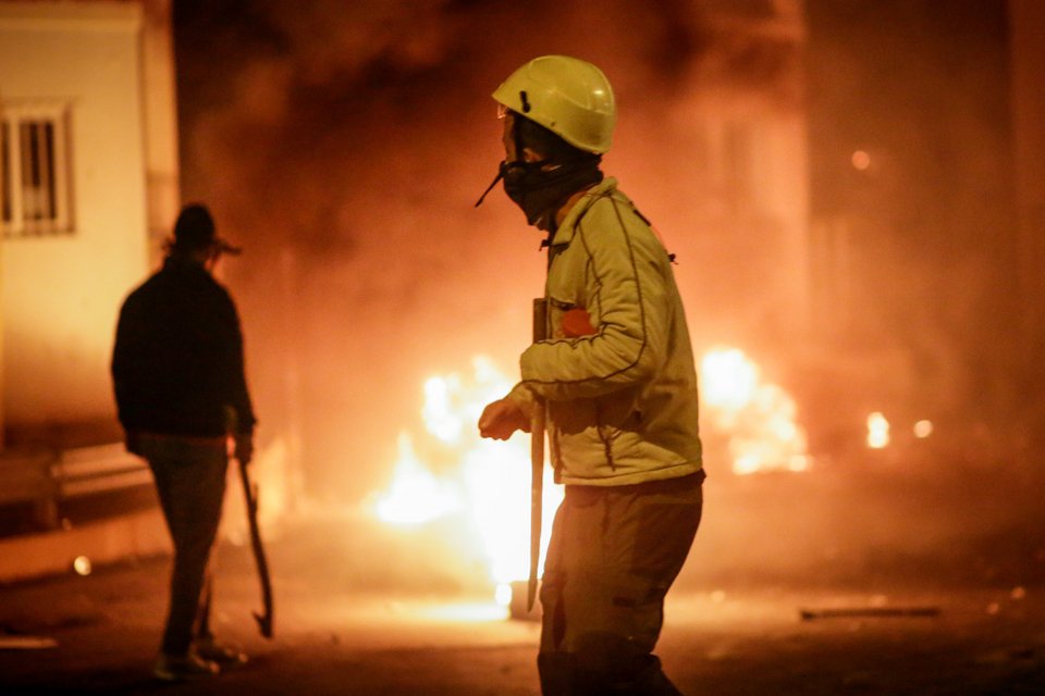Ανδρας κρατάει λοστάρι με φωτιές στο βάθος