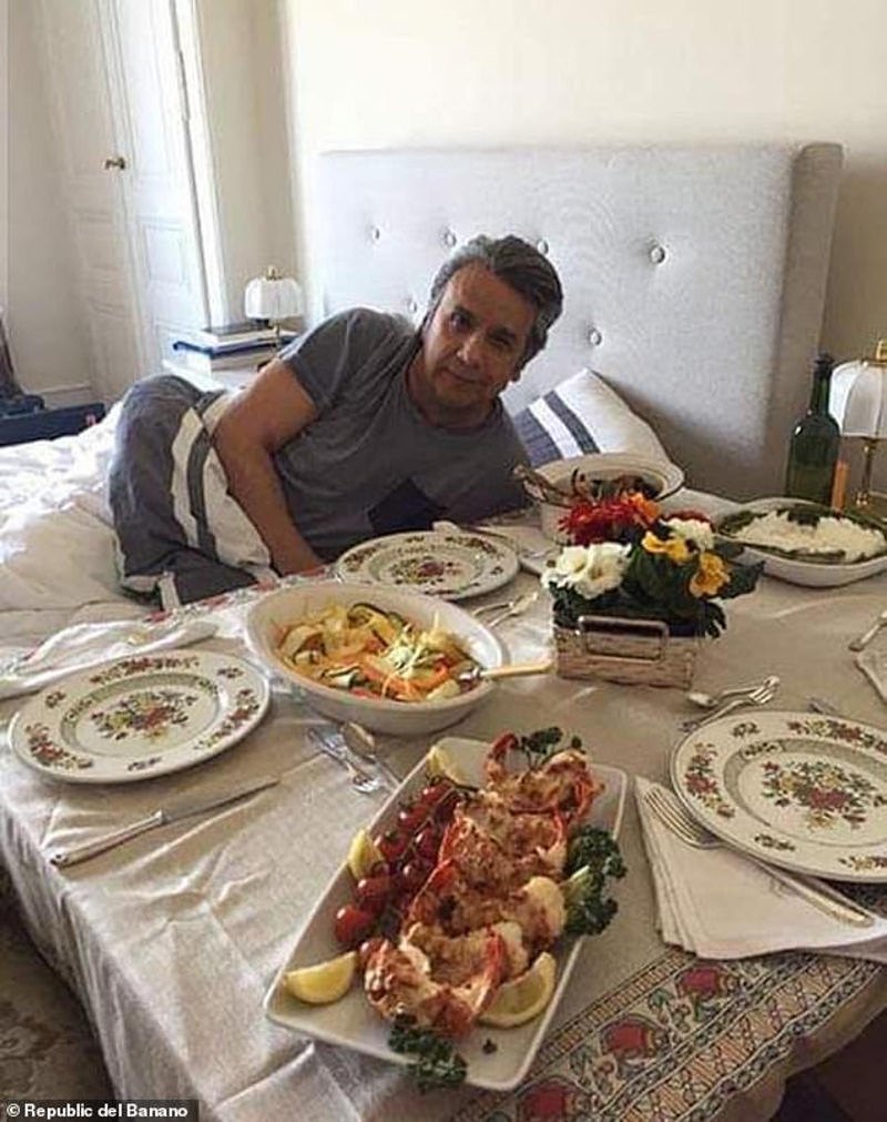 Ο Λένιν Μορένο ποζάρει στο κρεβάτι μπροστά από τραπέζι με πιάτα.