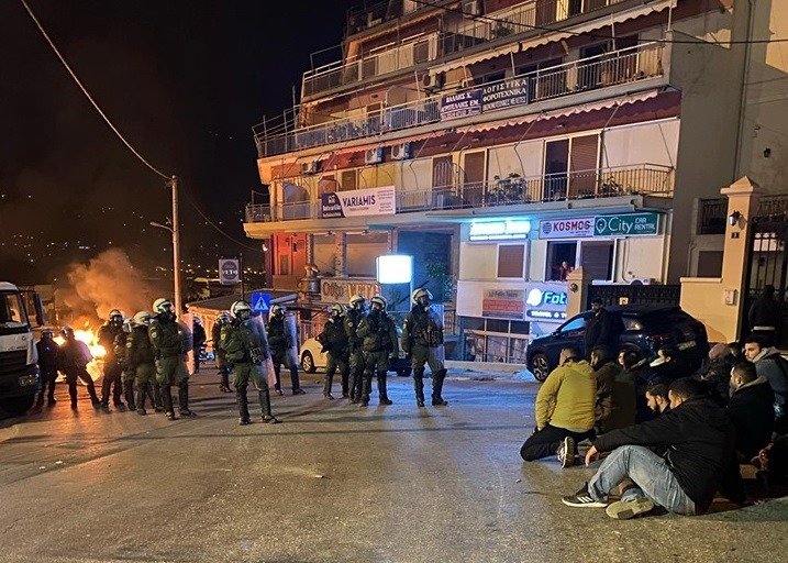 Νεαροί κάθονται στο οδόστρωμα υπό το βλέμμα των ΜΑΤ