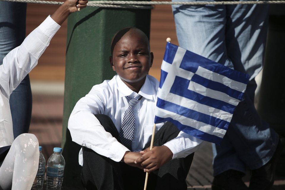 Με ανοιχτό γιακά και χαλαρό κόμπο γραβάτας μετά την παρέλαση ο μικρός μαθητής κρατά την ελληνική σημαία και κοιτάζει τον φωτογραφικό φακό