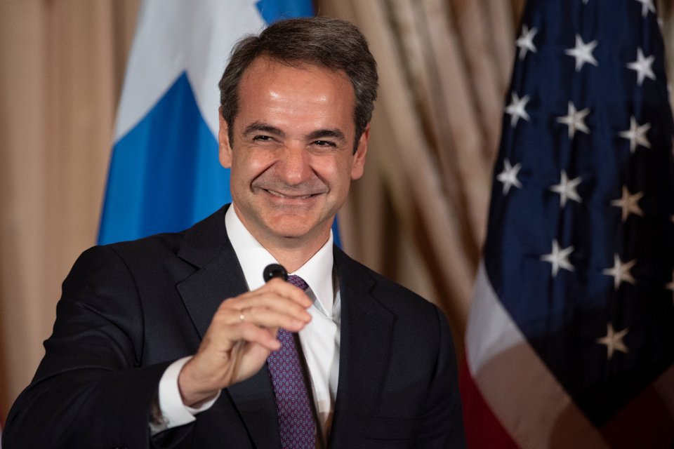 Ο Κυριάκος Μητσοτάκης χαμογελάει κρατώντας το μικρόφωνο