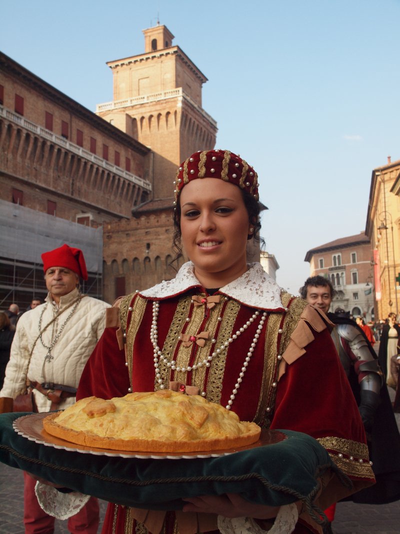 Γυναίκα με ρούχα εποχής δείχνει το Pasticcio Ferrarese, ένα τυπικό πιάτο της πόλης