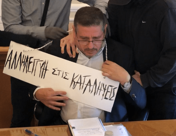 Στη φωτογραφία που ανέβασαν δείχνουν τον πρύτανη περικυκλωμένο από τους καταληψίες να του περνούν στο λαιμό μια ταμπέλα που γράφει «αλληλεγγύη στις καταλήψεις»