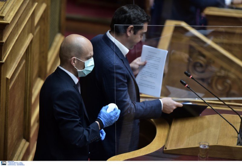 Ο Αλ. Τσίπρας κοιτάζει την ομιλία του όσο υπάλληλος της Βουλής καθαρίζει το προστατευτικό τζάμι