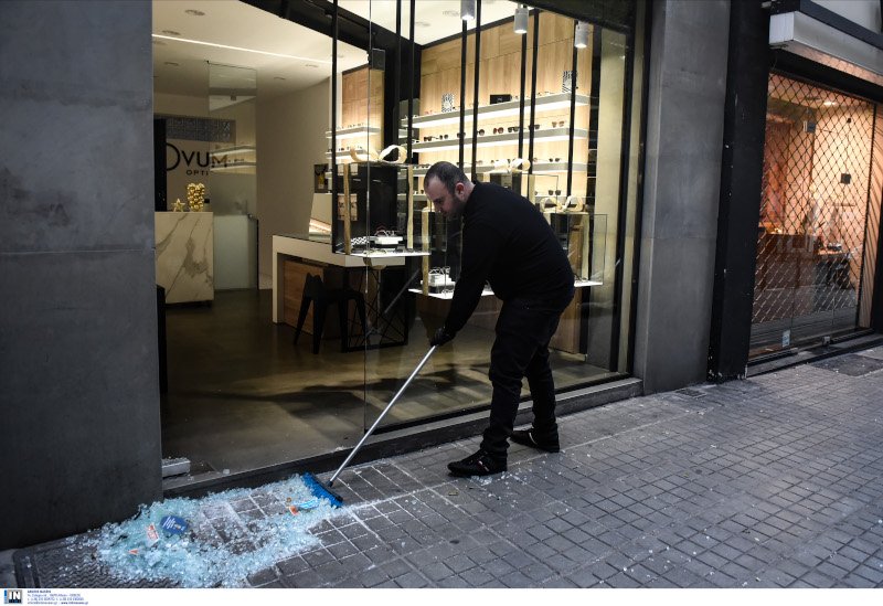 Ιδιοκτήτης καταστήματος μαζεύει τα θραύσματα από την σπασμένη τζαμαρία