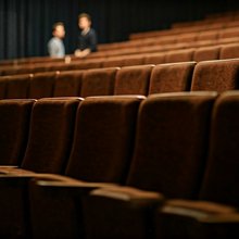 Καθίσματα θεάτρου και στο φόντο τρεις άνδρες