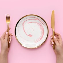 Γυναίκα με μαχαιροπίρουνα και άδειο πιάτο σε ροζ φόντο