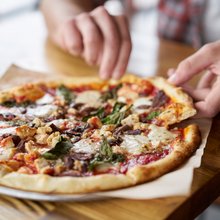 Χέρια άνδρα κόβουν κομμάτια μια πίτσα