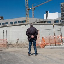 Ένας άνδρας «umarell» στέκεται με τα χέρια πίσω από την πλάτη, κοιτάζοντας πίσω από φράκτη έργων