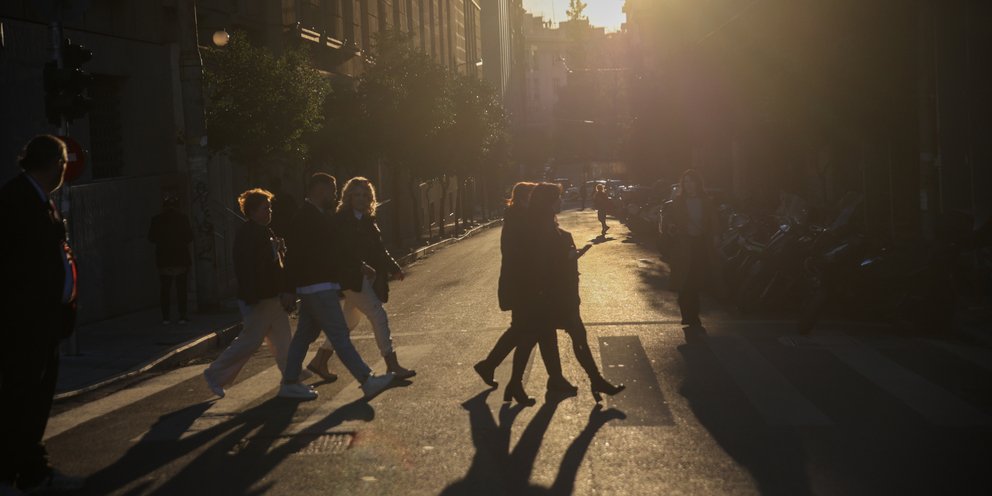 Άνθρωποι περπατούν σε δρόμο της Αθήνας υπό το φως του απογευματινού ήλιου 