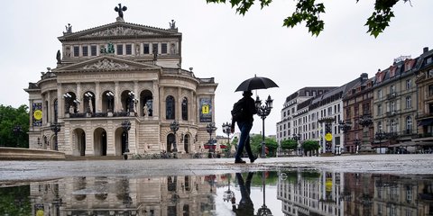 Ενας άνδρας με ομπρέλα περνά μπροστά από την παλιά όπερα στη Φρανκφούρτη
