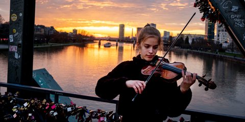 Μια νεαρή παίζει βιολί στις όχθες του ποταμού Μέιν στη Φρανκφούρτη το ηλιοβασίλεμα 