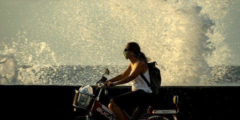 Μια γυναίκα με μάσκα σε ηλεκτρικό ποδήλατο περνά από κυματοθραύστη στην Αβάνα της Κούβας