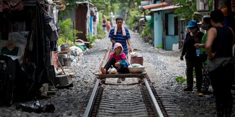 Ενας άντρας σπρώχνει ένα αυτοσχέδιο καρότσι με τη γυναίκα του στις γραμμές τρένου στη Μπανγκόκ