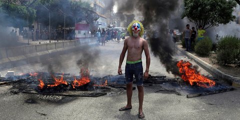 Λίβανος: Ενας αντικυβερνητικός διαδηλωτής με μάσκα κλόουν ποζάρει μπροστά από καμμένα ελαστικά 
