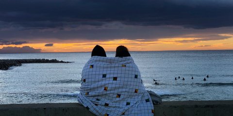 Ενα ζευγάρι τυλιγμένο με κουβέρτα στην παραλία της Βαρκελώνης παρακολουθεί την ανατολή του ήλιου στη Μεσόγειο