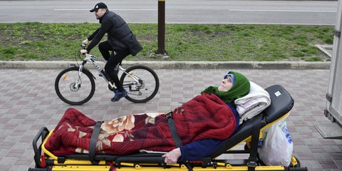 Μια ηλικιωμένη περιμένει στο φορείο να ξεκινήσει η διαδικασία εκκένωσης, στο Kramatorsk της Ουκρανίας, ενώ ένας ποδηλάτης περνάει τον δρόμο... /AP