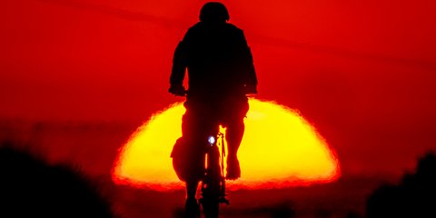 Ένας κάτοικος της Φρανκφούρτης πάει με το ποδήλατό του στη δουλειά, με φόντο έναν ολόλαμπρο ήλιο που ανατέλλει