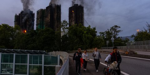 Κόσμος περπατάει με φόντο τα κτίρια που κάηκαν στο Χονγκ Κονγκ