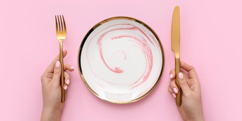 Γυναίκα με μαχαιροπίρουνα και άδειο πιάτο σε ροζ φόντο