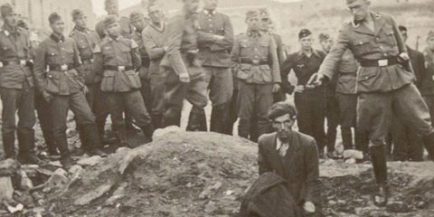 Ένας άνδρας γονατιστός στο χείλος ενός λάκκου γεμάτου πτώματα, κι ένας Γερμανός στρατιώτης με το χέρι σηκωμένο, το πιστόλι να ακουμπά σχεδόν τον σβέρκο του / WIKIPEDIA