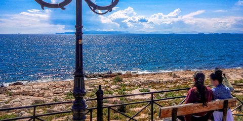 Δύο γυναίκες κάθονται σε παγκάκι και απολαμβάνουν τον ηλιόλουστο καιρό