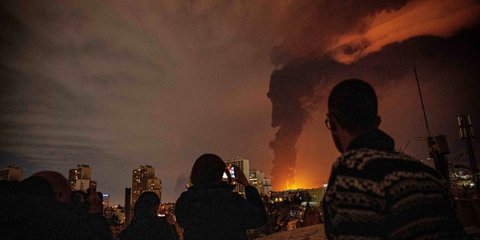 Κάτοικοι παρακολουθούν και φωτογραφίζουν τις φλόγες και τον καπνό που αναδύονται από μια εγκατάσταση αποθήκευσης πετρελαίου που χτυπήθηκε κατά τη διάρκεια των επιθέσεων που έπληξαν την πόλη κατά τη διάρκεια των αμερικανικών βομβαρδισμών στην Τεχεράνη