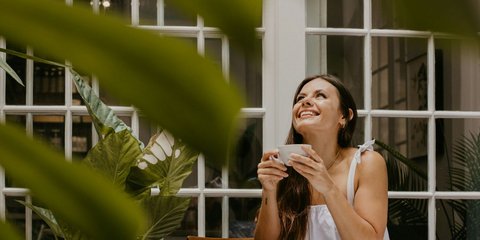 Νέα γυναίκα χαμογελαστή πίνει πρωινό καφέ σε βεράντα