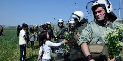 Μια προσφυγοπούλα στα Διαβατά προσφέρει ένα λουλούδι στους άνδρες των ΜΑΤ -Φωτογραφία: Intimenews