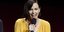 H μελαχρινή Σαρλίζ Θερόν με κίτρινο φόρεμα χαμογελάει κρατώντας το μικρόφωνο.