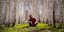 Γυναίκα κάθεται στο χώμα και κοιτάζει ψηλά τον ουρανό στο δάσος