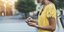 Γυναίκα με κίτρινο φόρεμα κοιτάζει το κινητό της στο δρόμο