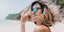 Ξανθιά γυναίκα στην παραλία με γυαλιά ηλίου και λευκό τοπ 