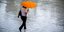 Μια γυναίκα περπατά στη βροχή, στο κέντρο της Αθήνας, κρατώντας ομπρέλα