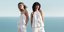 Δύο γυναίκες ντυμένες στα λευκά ποζάρουν πάνω σε βράχο με θέα θάλασσα