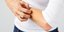 Γυναίκα με λευκή μπλούζα και τζιν ξύνει το χέρι της 