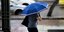 Μια γυναίκα περπατά στη βροχή κρατώντας ομπρέλα